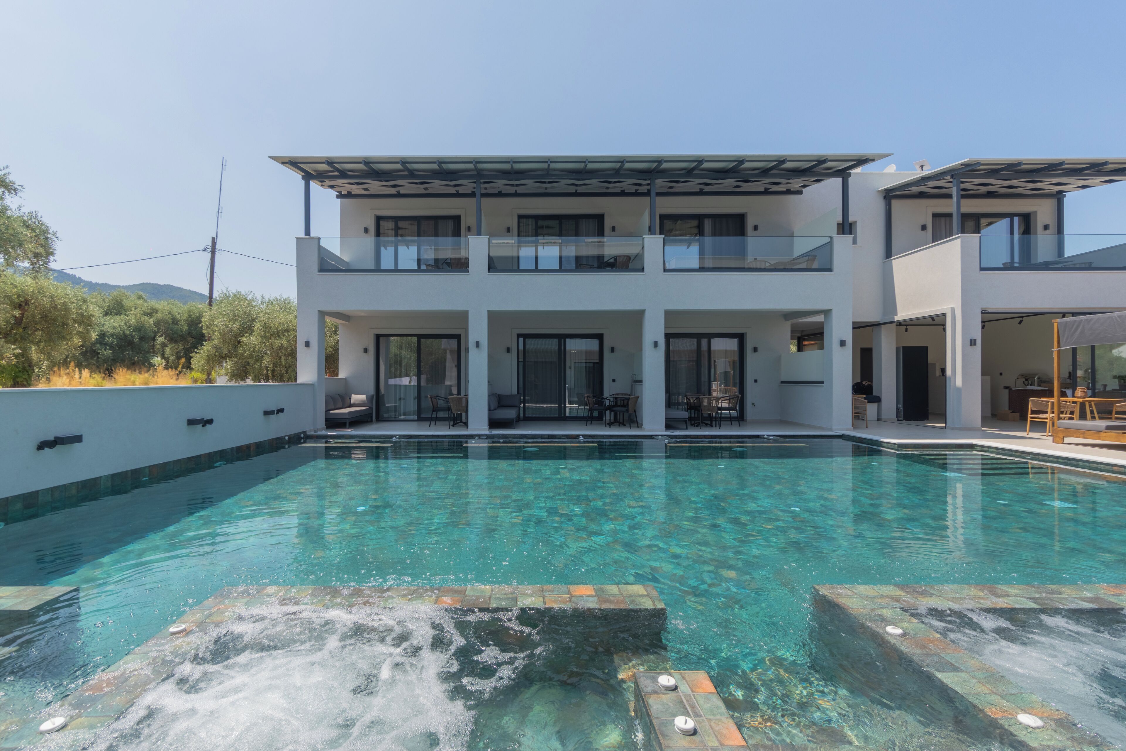 Ein modernes, zweistöckiges Haus mit Swimmingpool, Sitzgelegenheiten im Freien und Whirlpool.