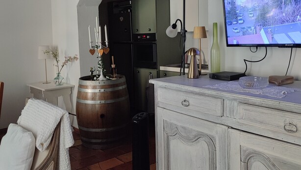 A rustic kitchen with a wooden barrel, a white cabinet, and a television displaying a residential area.