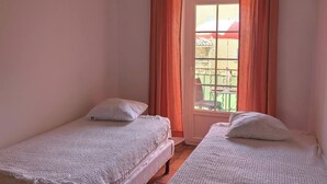 A room with two single beds, a hanging lamp, and a window with curtains.