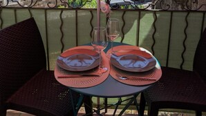 A table set for two under a red umbrella on a balcony with a view of buildings and a car in the background.