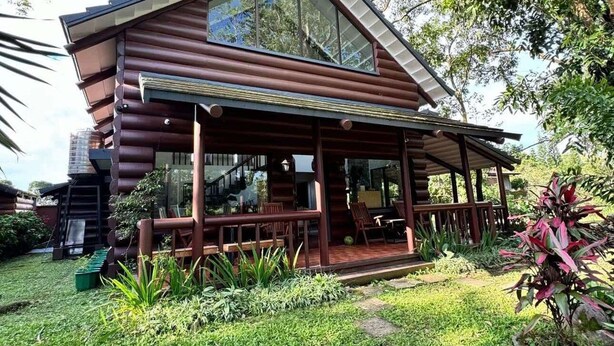 Una cabaña de madera con un porche cubierto, un pequeño jardín y una escalera que lleva a la entrada.
