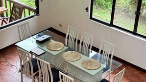 Un comedor con mesa de vidrio, sillas blancas y individuales tejidas.