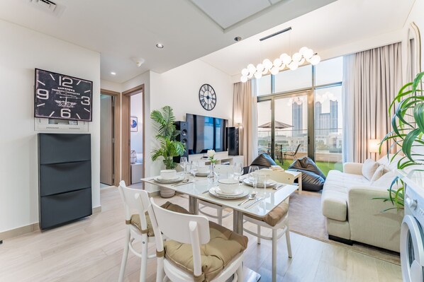 A modern dining area with a table set for four, a clock on the wall, and a sofa in the background.
