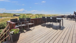 A wooden deck with outdoor seating, overlooking a beach and dunes. - 4 Person Holiday Home on a Holiday Park in Fano (Fano)
