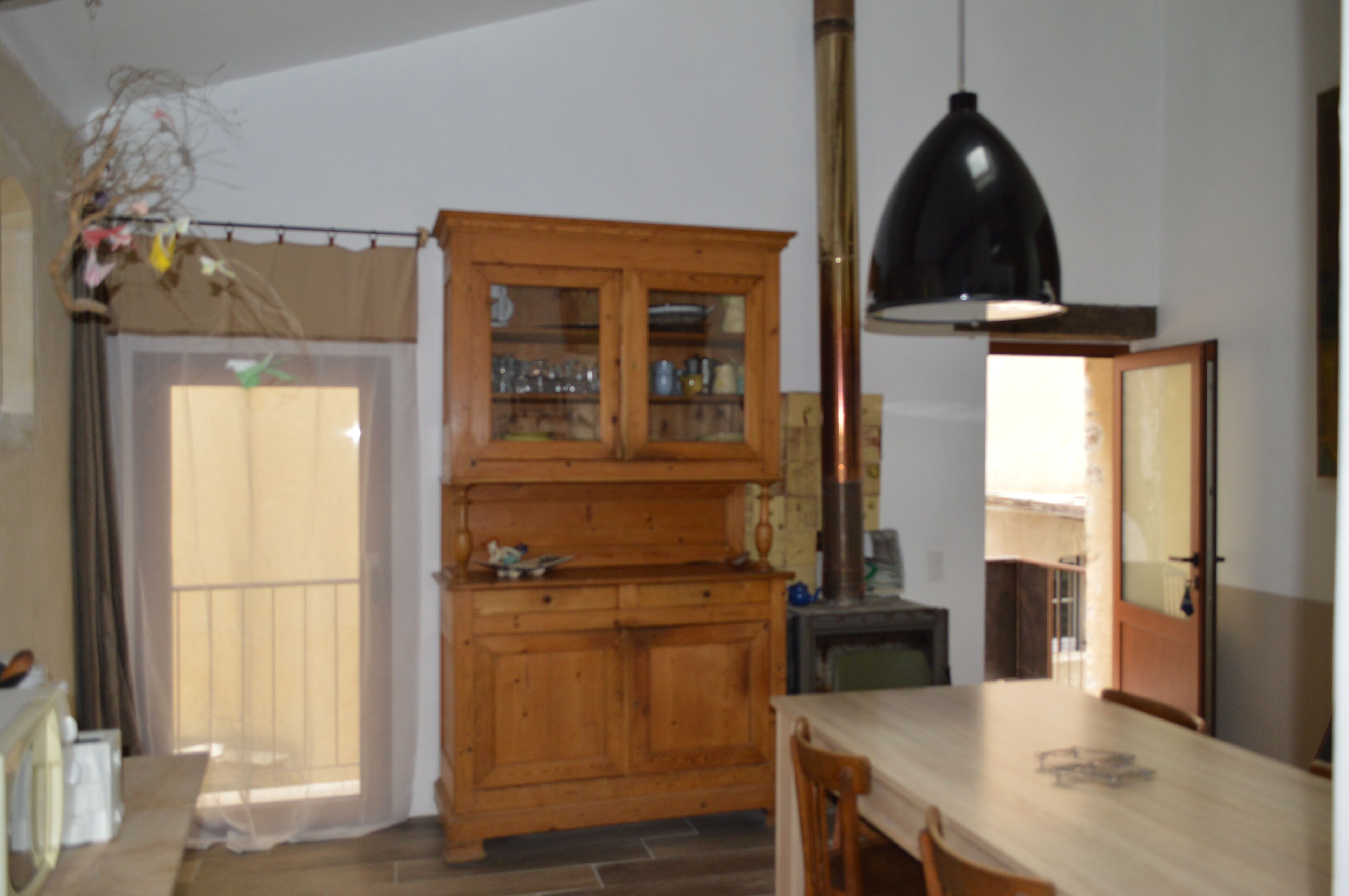 Una cocina con armarios de madera, una mesa, sillas, una lámpara colgante y vistas a través de una ventana.