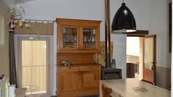 Una cocina con armarios de madera, una mesa, sillas, una lámpara colgante y vistas a través de una ventana.