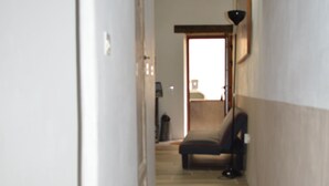 A narrow hallway with wooden beams on the ceiling, a bench, and a door leading to another room. - Small artist's house (Saint-Étienne-les-Orgues)