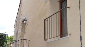 A building with a balcony, a door, and a window with a metal railing. - Small artist's house (Saint-Étienne-les-Orgues)