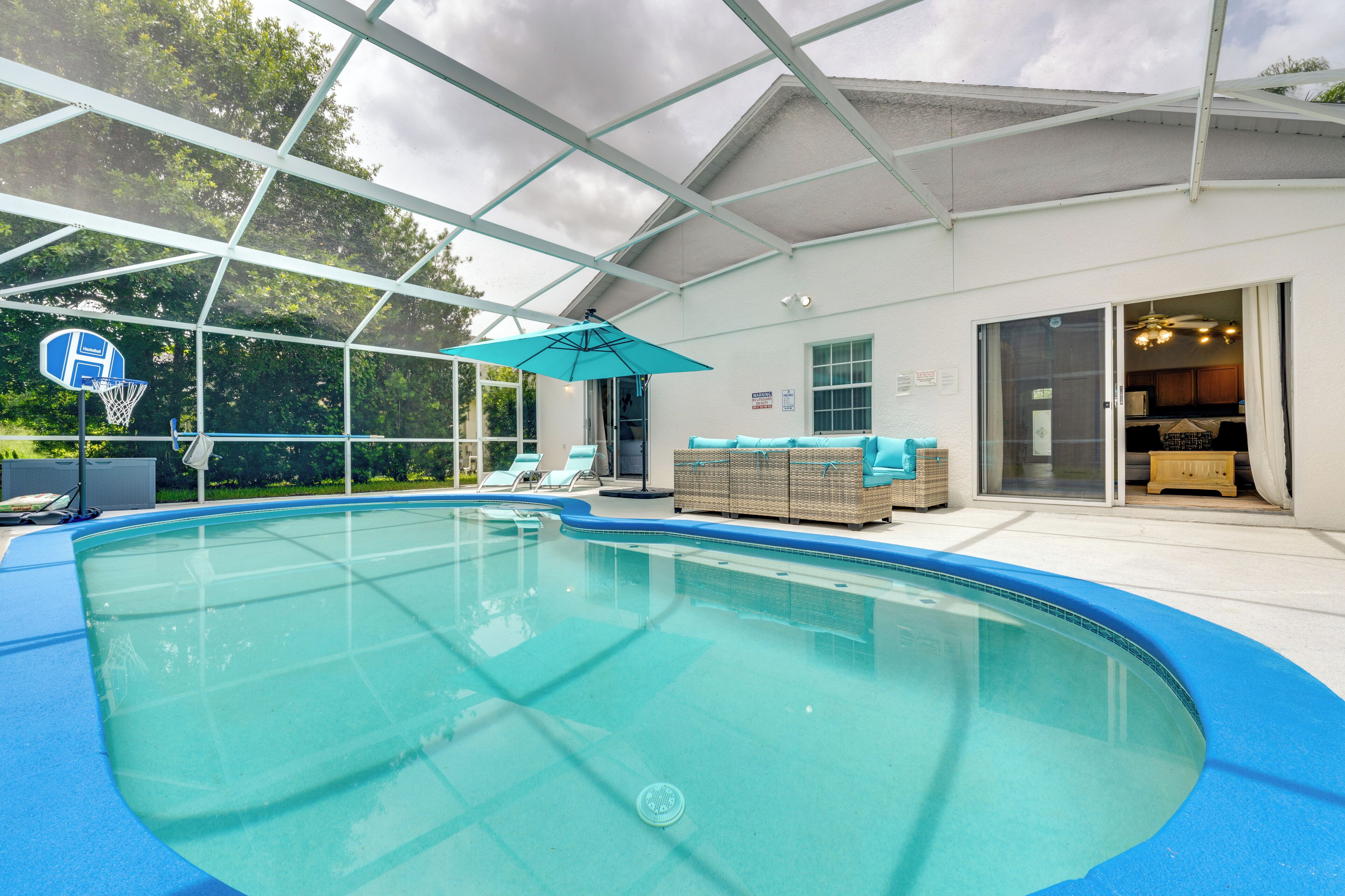 An indoor swimming pool with a glass ceiling, a basketball hoop, and lounge chairs.