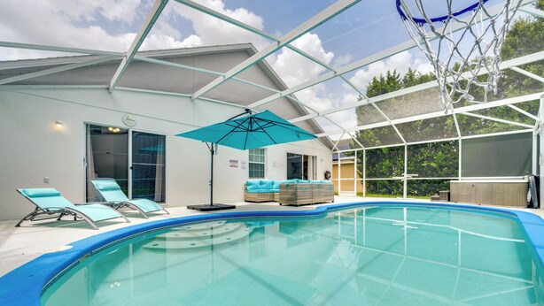 Una piscina interior con agua azul cristalina, una zona techada con sillones de descanso y un aro de baloncesto.