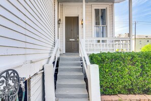A white wooden house with a front porch, a set of concrete steps leading to a door, and a hedge in the foreground. - 1 Mi to Pleasure Pier: Golden-age Getaway! (Galveston)