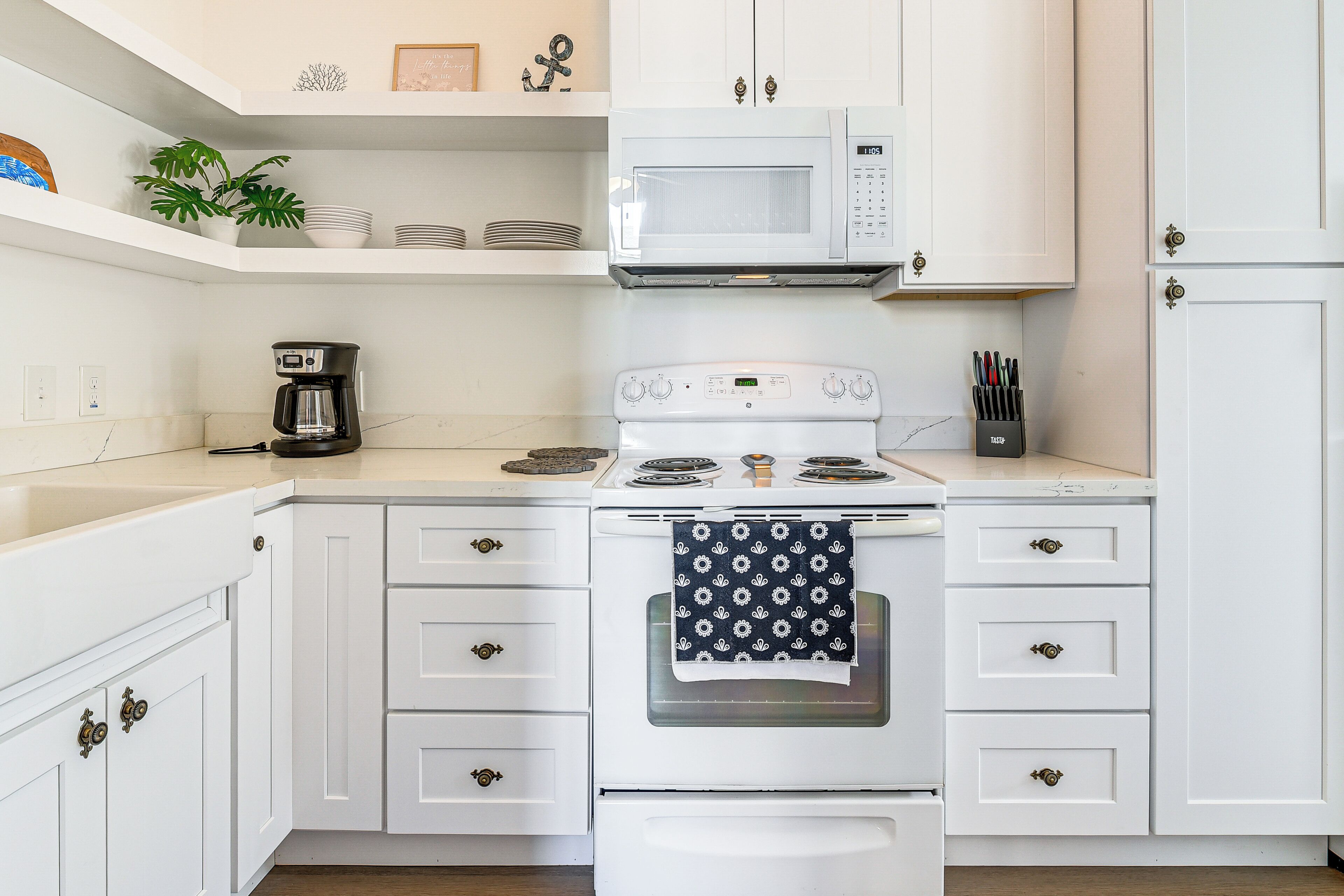 A kitchen with white cabinets, a white stove, a microwave, and a coffee maker.