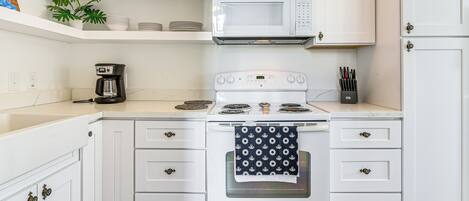 A kitchen with white cabinets, a white stove, a microwave, and a coffee maker.