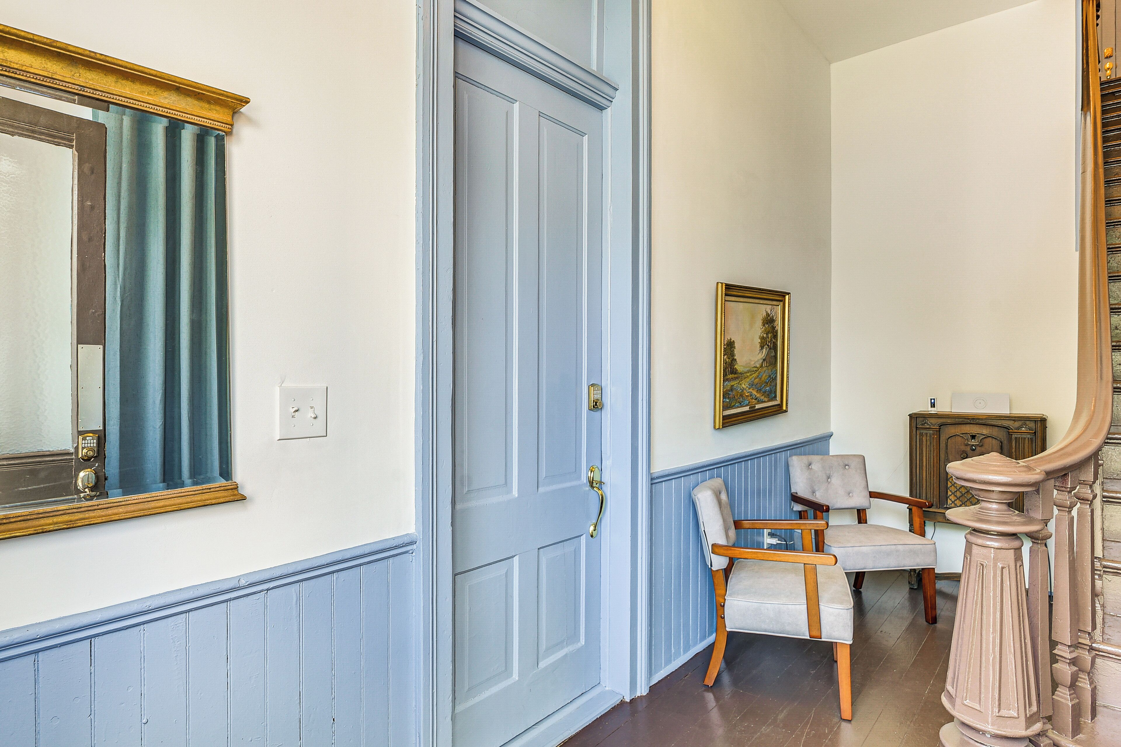 Ein Flur mit einer blauen Tür, einem Spiegel, einem Stuhl und einem Bild an der Wand.