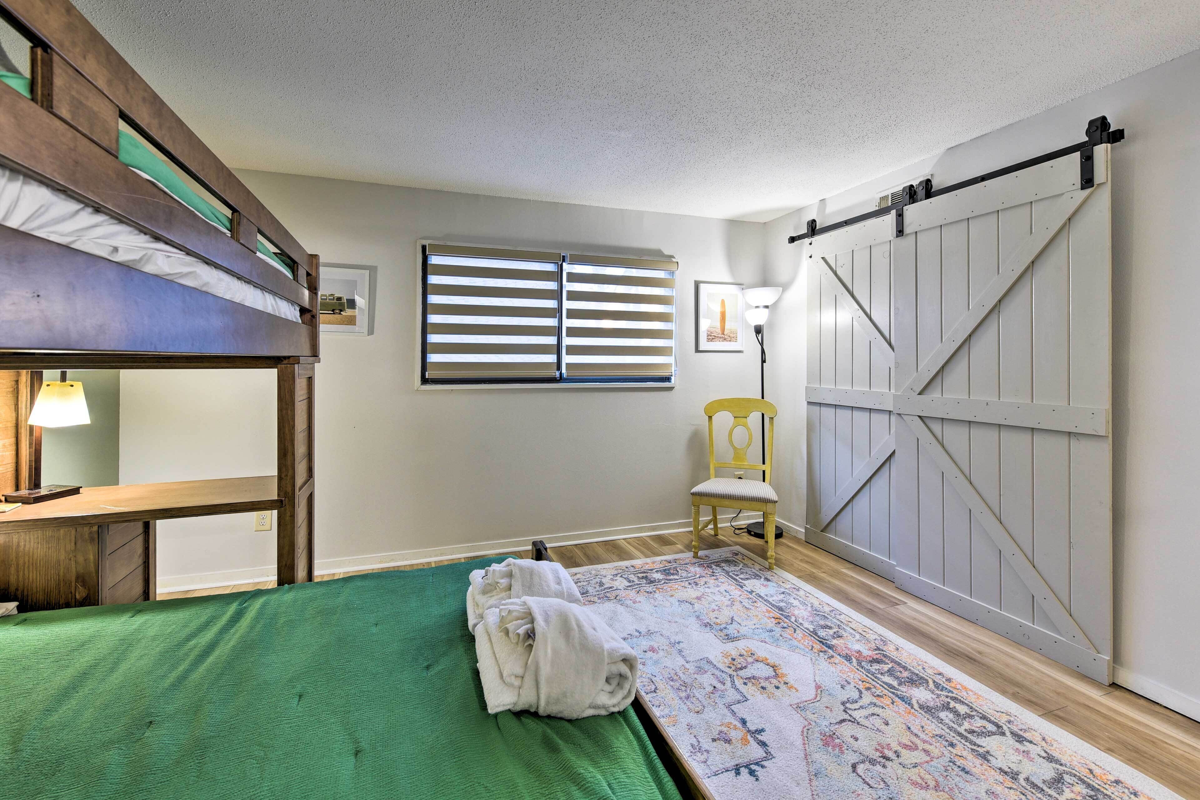 Une chambre avec un lit superposé, un bureau, une chaise, une grande porte coulissante et une fenêtre avec des stores.