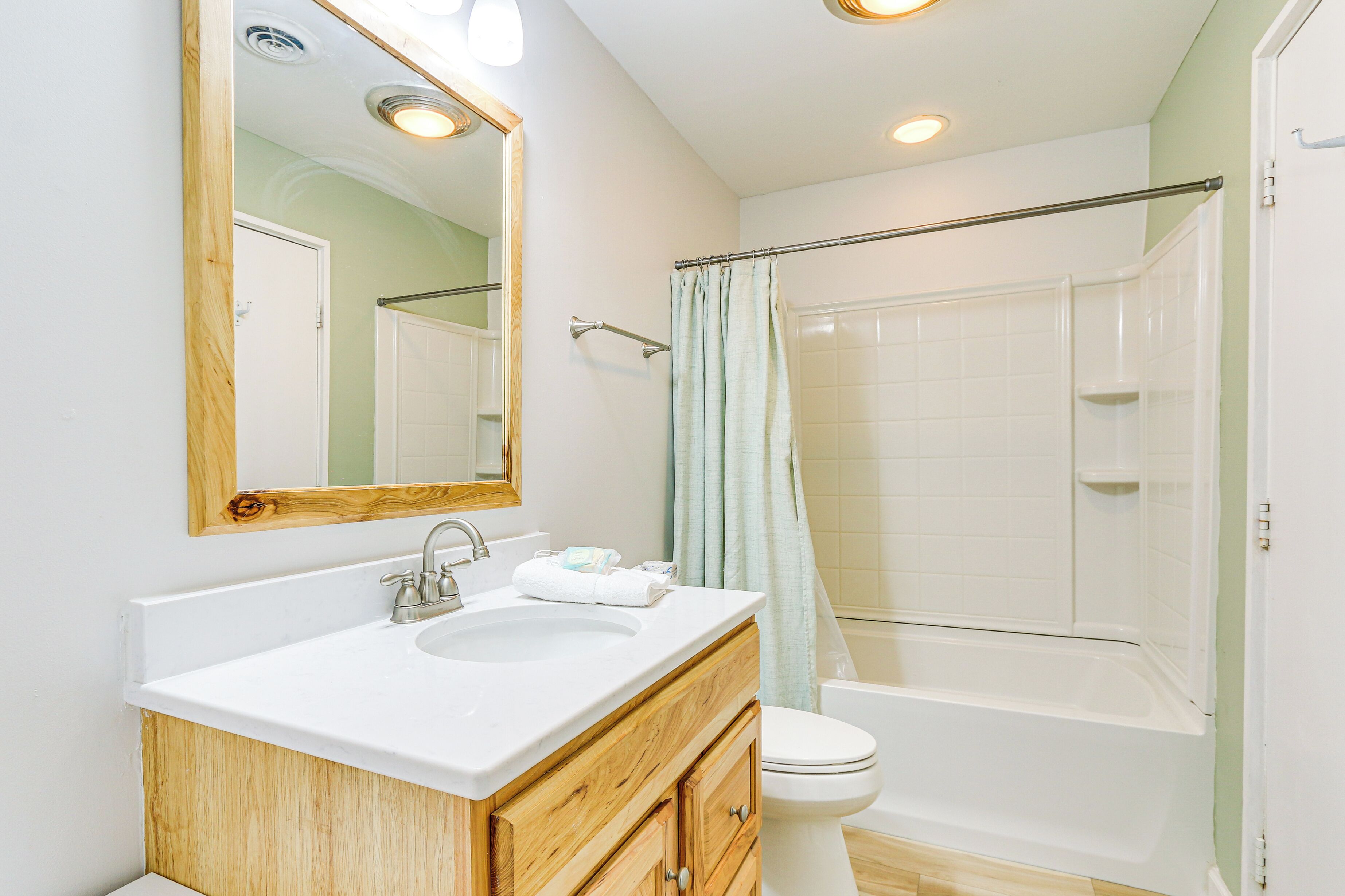 Une salle de bain avec un meuble-lavabo en bois, un lavabo blanc et une douche dotée d’une porte en verre.