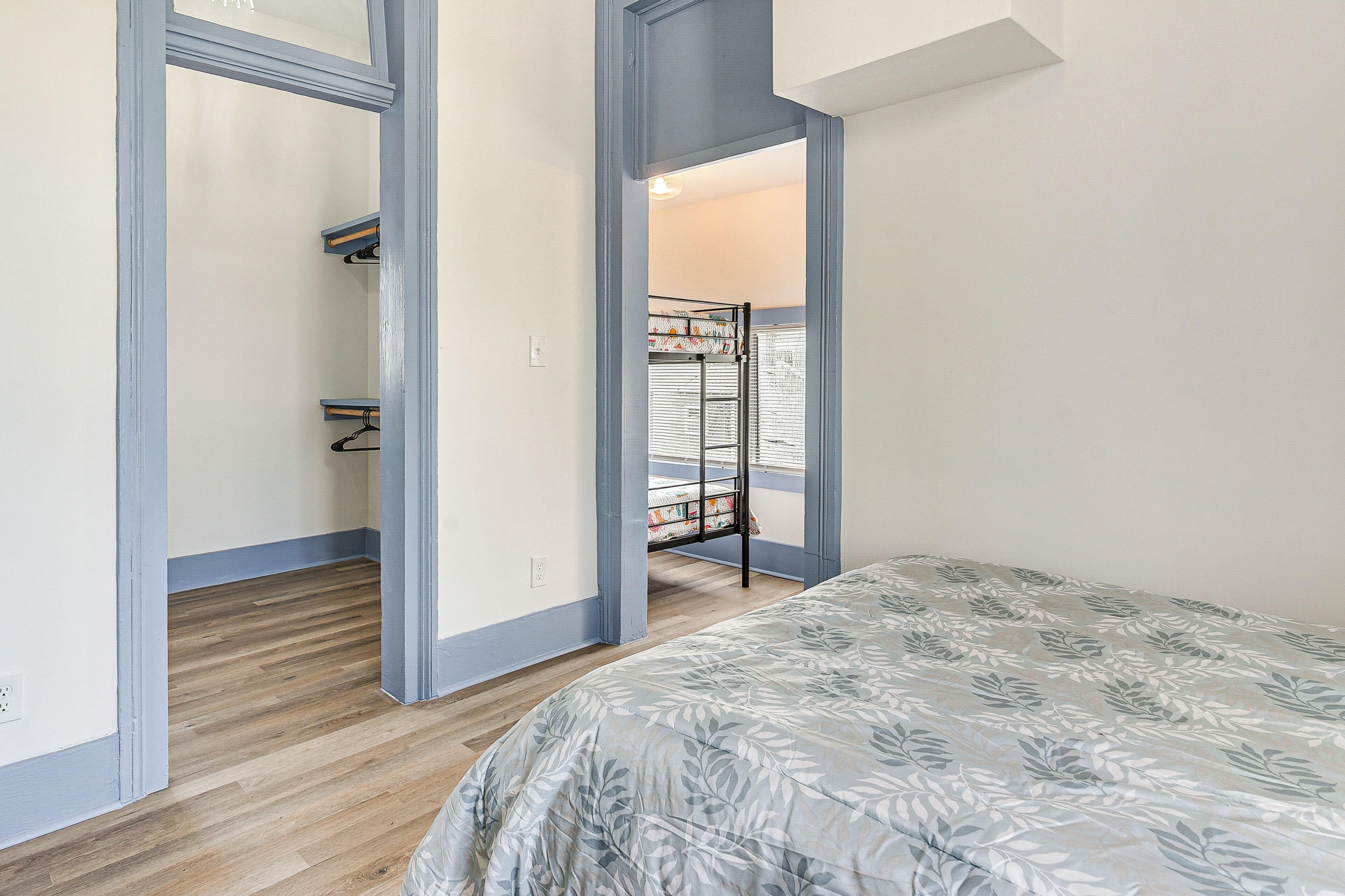 A bedroom with a bed, wooden flooring, and a view of a balcony with a clothes drying rack.