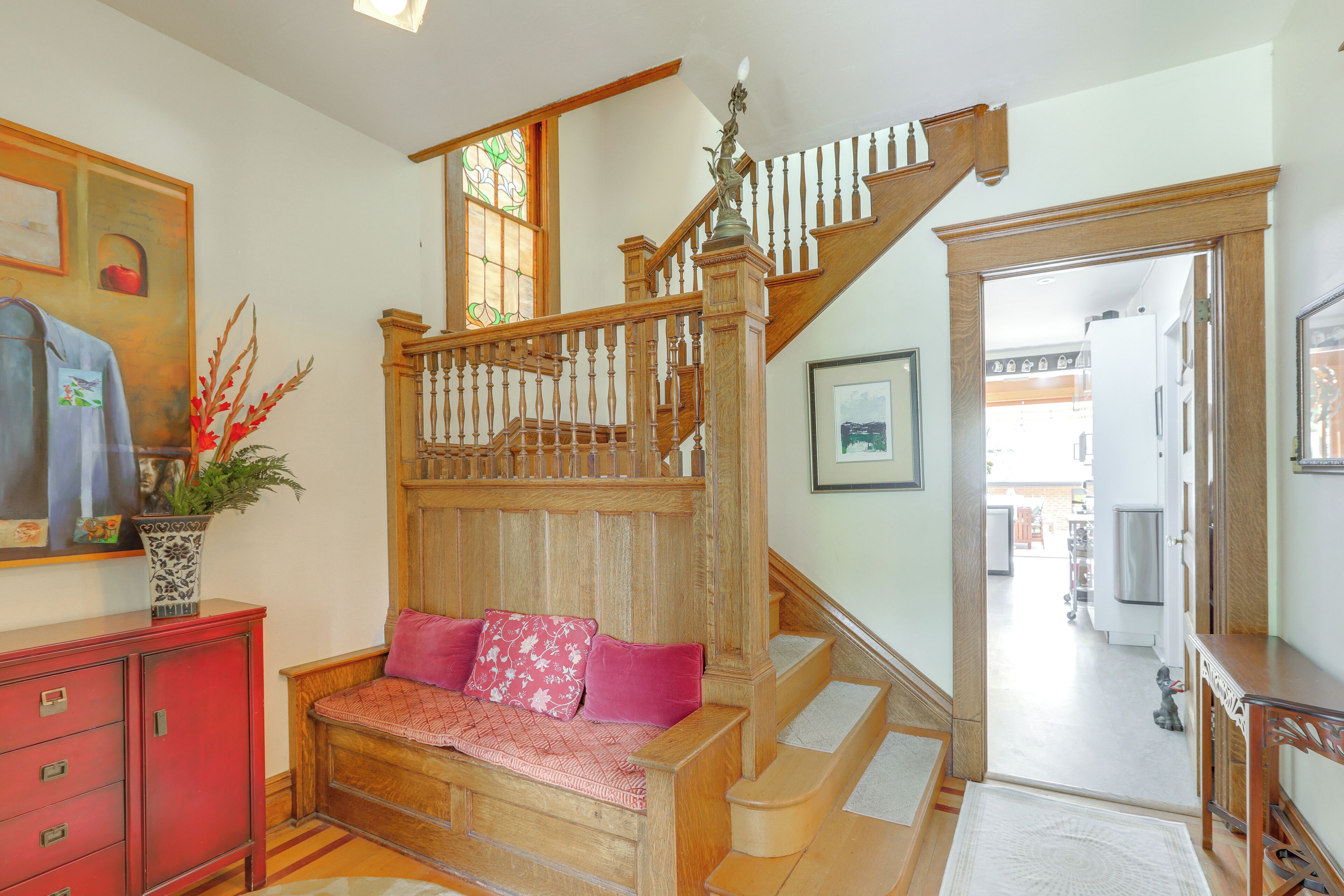 A wooden staircase with a bench at the bottom, a red cabinet, and a plant.