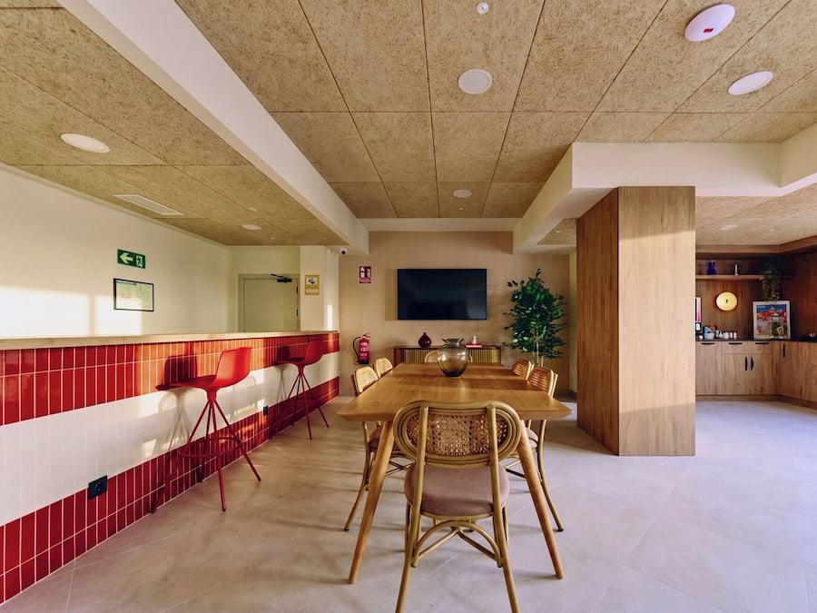 Un comedor de hotel con una larga mesa de madera, sillas rojas, un televisor y una planta.