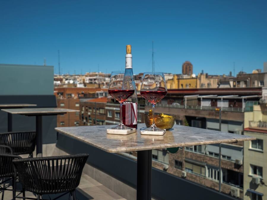 Una terraza en la azotea con una mesa dispuesta para dos personas, una botella de vino y dos copas de vino tinto.