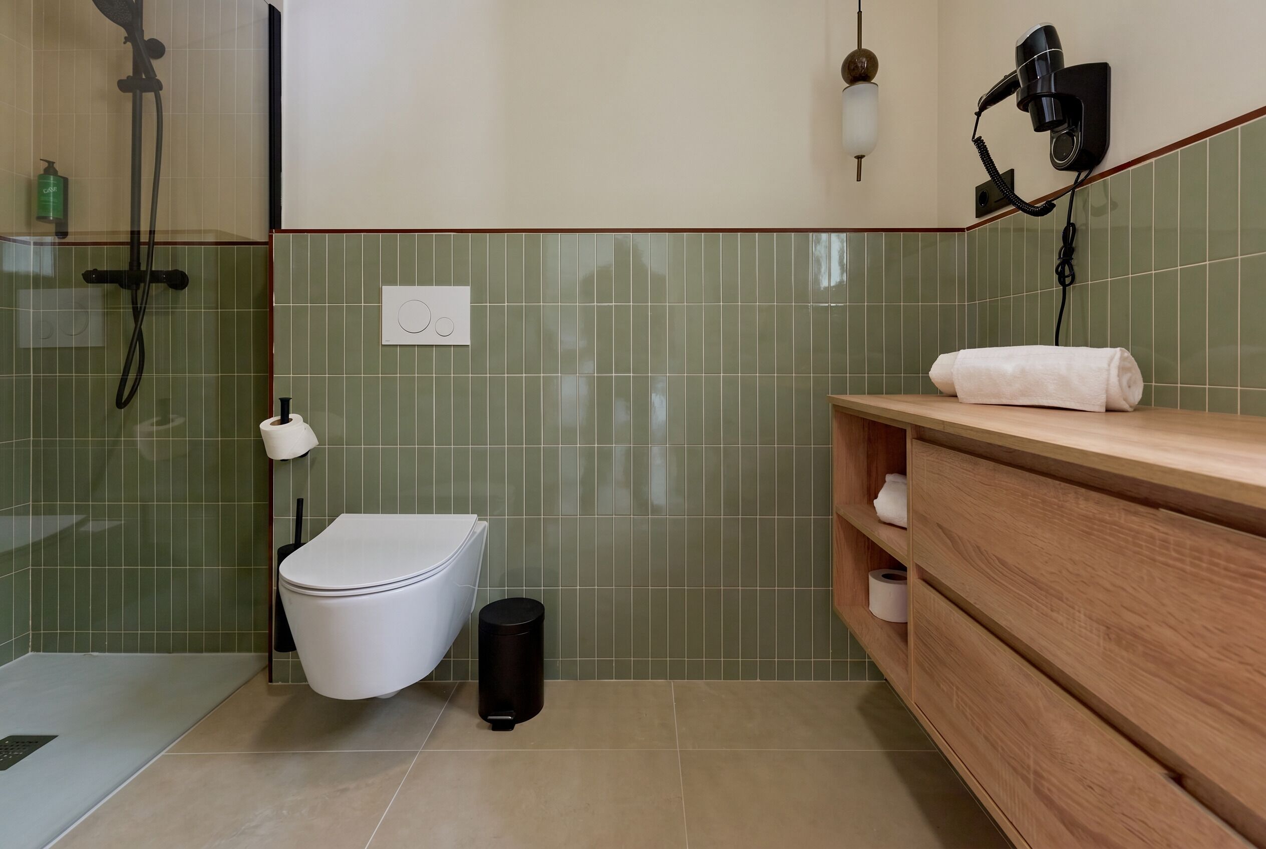Une salle de bain équipée de toilettes, d’une douche, d’une serviette posée sur le comptoir et d’un sèche-cheveux fixé au mur.