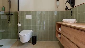 Une salle de bain équipée de toilettes, d’une douche, d’une serviette posée sur le comptoir et d’un sèche-cheveux fixé au mur.