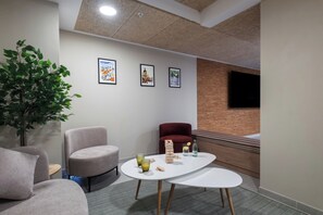 Una habitación moderna con una mesa redonda, dos sillas, un sillón rojo, una planta en maceta y cuadros en la pared.