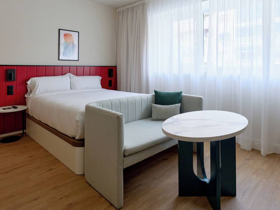 Habitación de hotel con cama, sofá, una mesita y un cuadro en la pared.