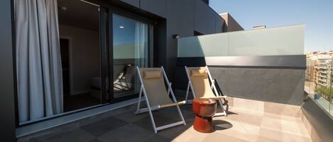 En moderne balkon med to loungesæder, et lille bord og en glasdør til et indre rum.