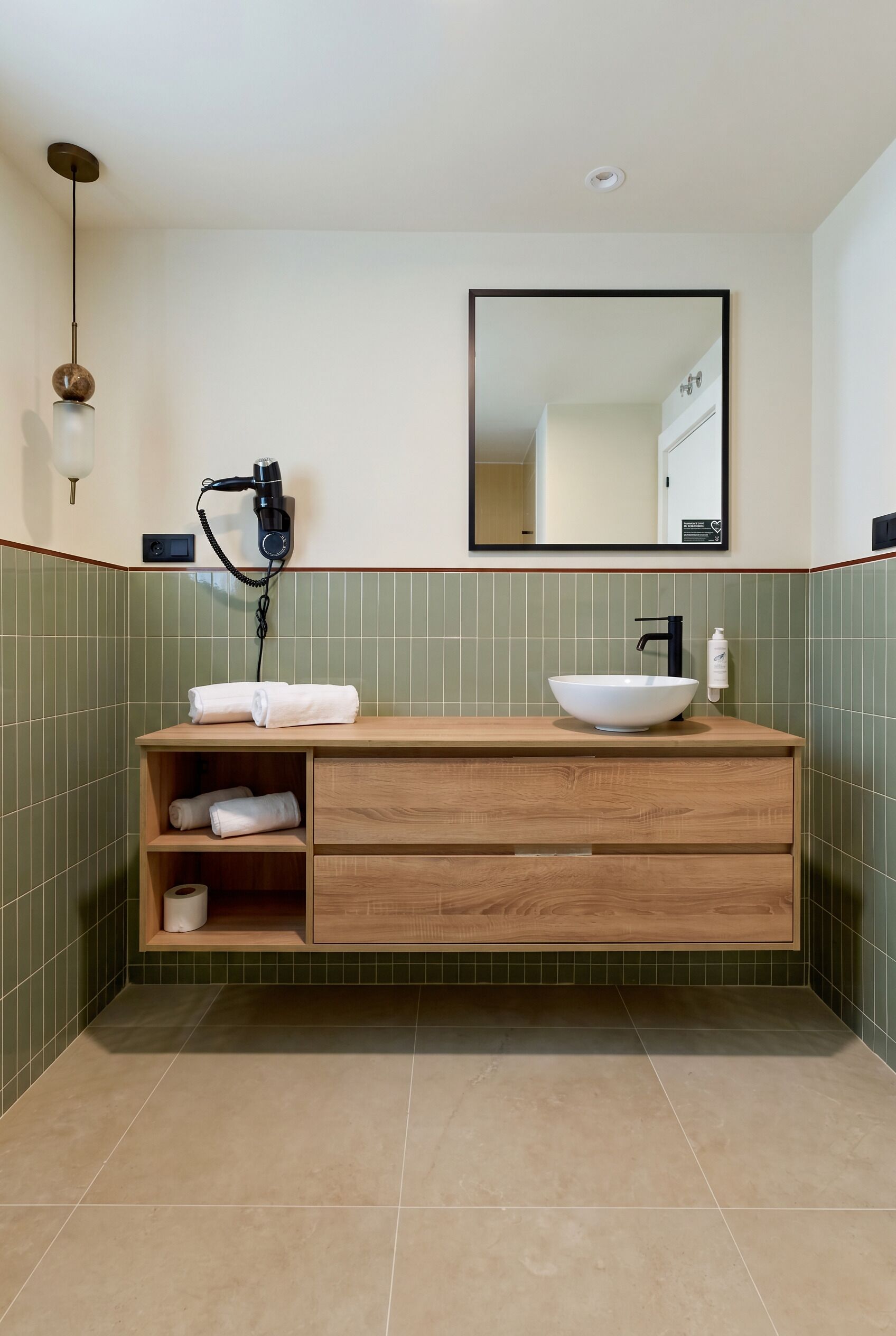A bathroom with a wooden vanity, a white sink, a hairdryer, and a mirror.