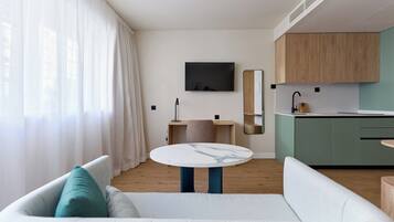 A modern living room with a sofa, a round table, a TV, and a kitchen area with wooden cabinets.