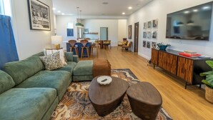 A modern living room with a green sofa, a coffee table, and a dining area in the background. - Bold, Fun Getaway near Lake, Zoo, Downtown (Michigan City)
