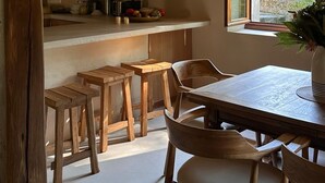 Una cocina rústica con vigas de madera, un ventanal grande y una zona de comedor con taburetes y sillas.