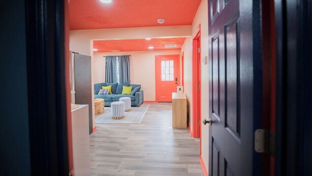 A hallway leading to a living area with a sofa, ottomans, and a door. - Stylish 3BR Getaway • Near Downtown & Restaurants (Richmond)