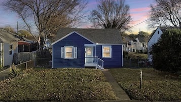 Une petite maison de plain-pied avec un porche à l’avant et un chemin menant à l’entrée.