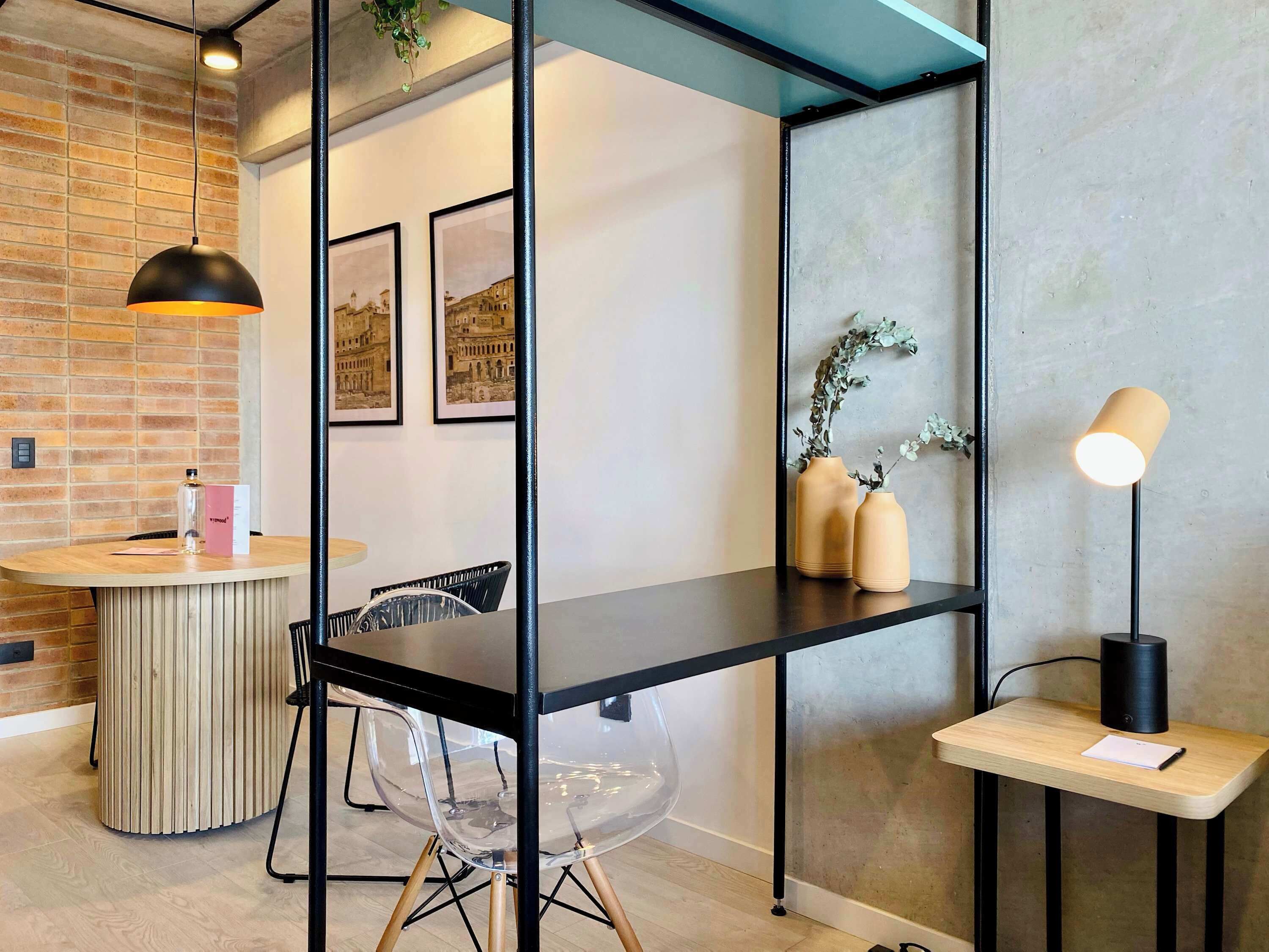 Interior modern amb una taula de fusta, cadira de plàstic transparent, estructura de metall negre i una petita estant amb gerros i una làmpada.