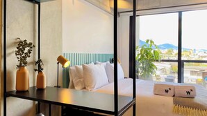 A modern hotel room with a bed, a desk, and a chair. There are two potted plants on the desk.