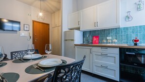 Una cocina moderna con armarios blancos, horno empotrado y microondas. Hay una mesa de comedor con platos, vasos y cubiertos.