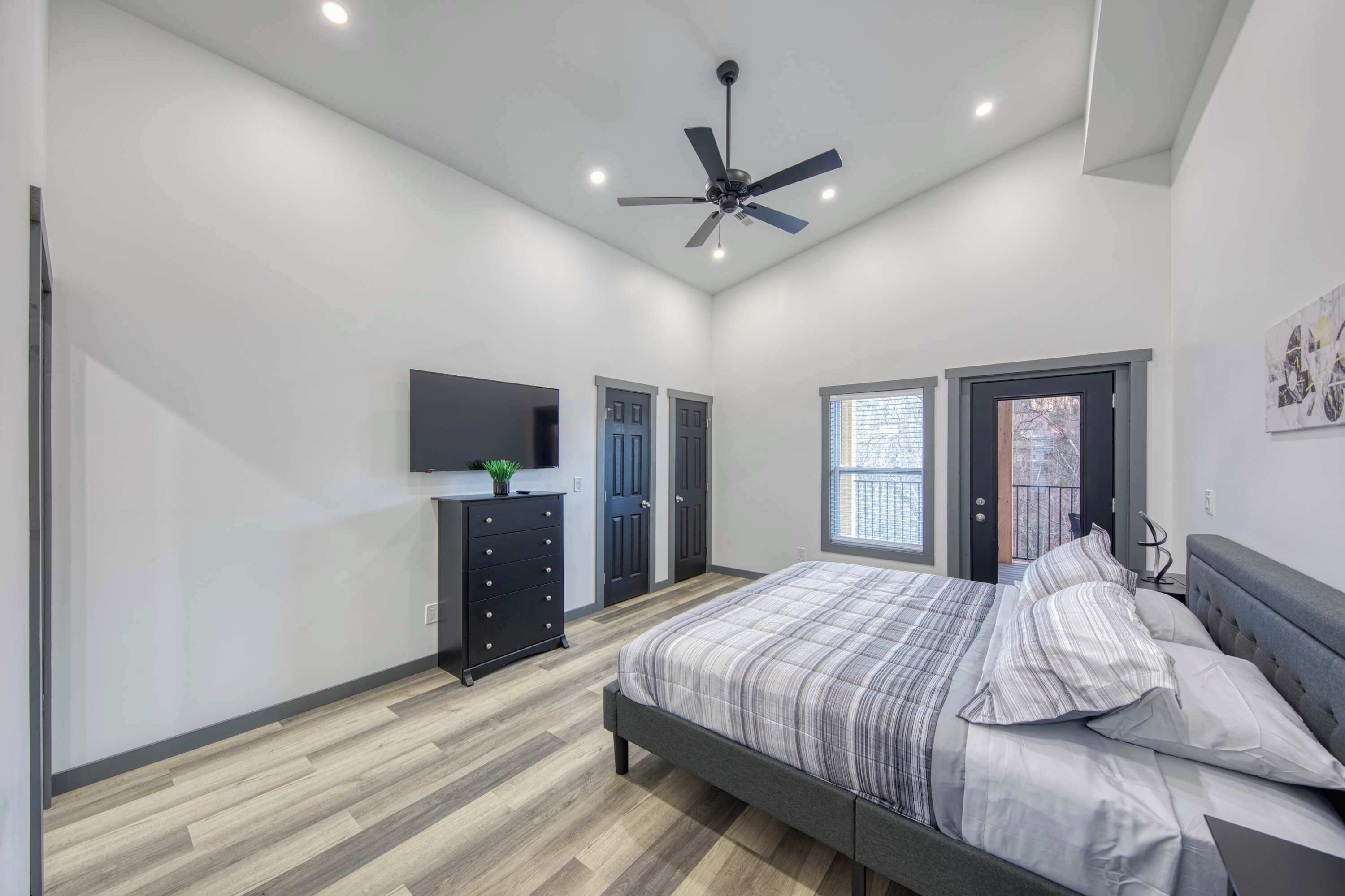 Une chambre à coucher avec un lit, un ventilateur de plafond, une commode, un téléviseur et une fenêtre.