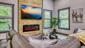 A modern living room with a fireplace, a large flat-screen TV, and a comfortable sofa. - Bearfoot Getaway - New Lux Cabin Hot Tub Pool (Gatlinburg)