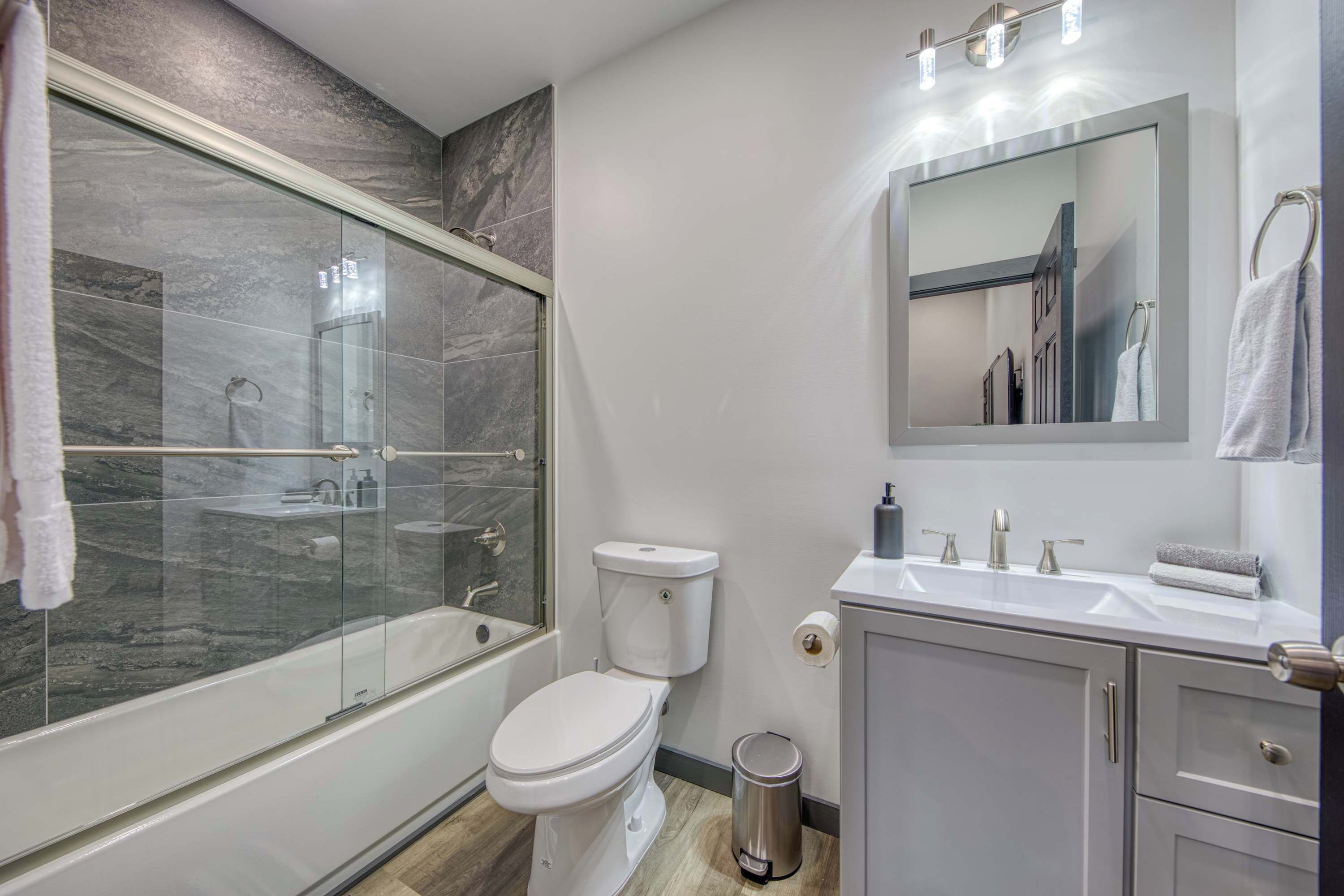 A modern bathroom with a glass-enclosed shower, a white toilet, and a sink with a mirror above it.