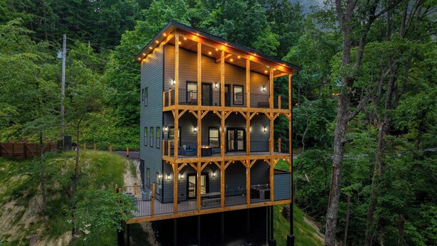 A multi-story wooden cabin with balconies, surrounded by dense forest. - Bearfoot Getaway - New Lux Cabin Hot Tub Pool (Gatlinburg)