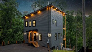 A modern two-story cabin with a balcony, surrounded by trees and a starry night sky. - Bearfoot Getaway - New Lux Cabin Hot Tub Pool (Gatlinburg)