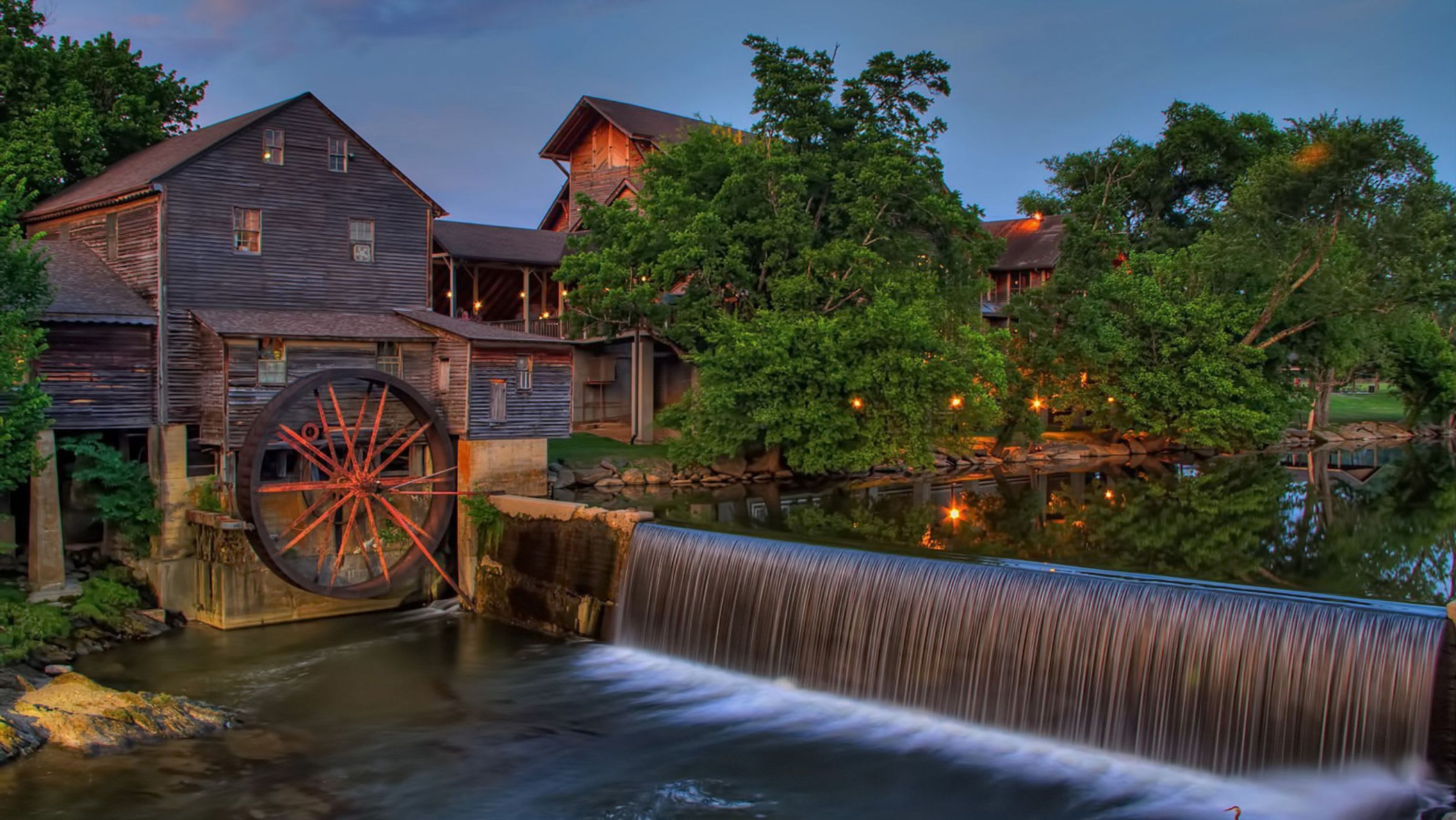 A historic building with a large water wheel, a wooden structure, and a small waterfall.