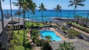 Un resort con piscina rodeada de palmeras, vista a la playa y zona de estacionamiento.