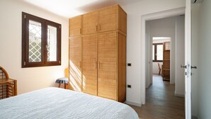 A bedroom with a large bed, a wardrobe, a window, and a door leading to another room.