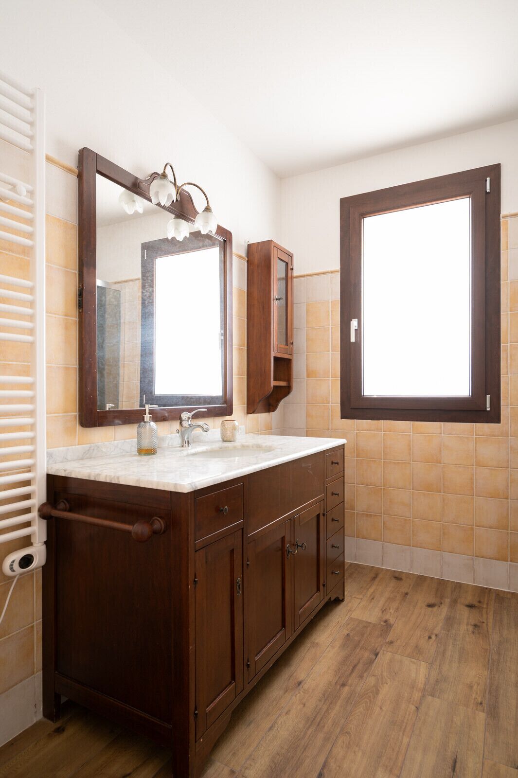 A bathroom with a wooden vanity, a large mirror, and a window.