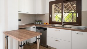 A modern kitchen with white cabinets, a wooden countertop, a built-in dishwasher, and a window with a lattice design.
