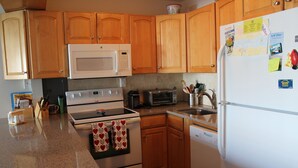 A kitchen with wooden cabinets, a microwave, stove, oven, toaster, sink, and refrigerator.
