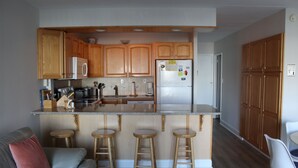 A compact kitchen with wooden cabinets, a stainless steel refrigerator, a built-in oven, and a bar stool seating area.